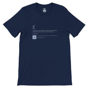 Könnte beinhalten: Ein marineblaues T-Shirt mit einem weißen traurigen Gesicht und dem Text: "Ihr Gerät ist auf ein Problem gestoßen und muss neu gestartet werden. Wir sammeln gerade einige Fehlerinformationen und starten dann für Sie neu. 0 % abgeschlossen"