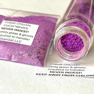 Puede incluir: Un frasco de vidrio transparente y una bolsa de plástico llena de polvo de cloruro de cobalto púrpura vibrante. La bolsa tiene una etiqueta con instrucciones de seguridad. Una segunda etiqueta cerca del frasco también proporciona advertencias de seguridad.