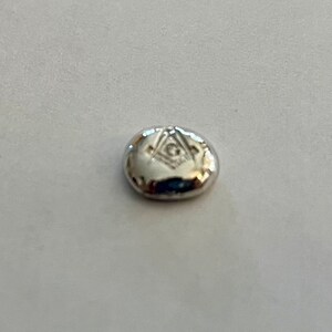 K&ouml;nnte beinhalten: Ein silberfarbener, ovaler Anh&auml;nger mit einem eingravierten Freimaurer-Symbol.