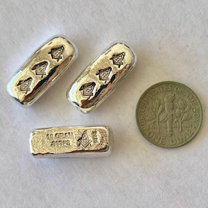 May include: Three silver bars with a Masonic symbol and a dime. Two bars have the symbol repeated three times. The third bar is stamped with "10 GRAM .999 FG" and the Masonic symbol. The dime is a United States coin.