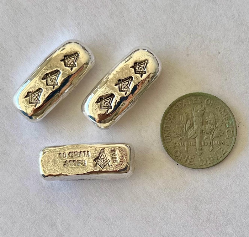 May include: Three silver bars with a Masonic symbol and a dime. Two bars have the symbol repeated three times. The third bar is stamped with "10 GRAM .999 FG" and the Masonic symbol. The dime is a United States coin.