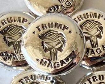 May include: A collection of silver-colored round coins with the words "TRUMP" and "MAGA" printed on them. Each coin features a skull with a mohawk.