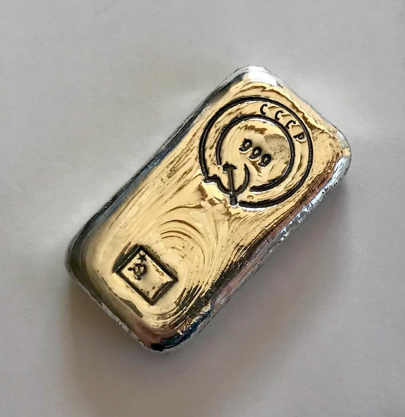 May include: A silver bar with a gold-colored inscription that reads "СССР 999".
