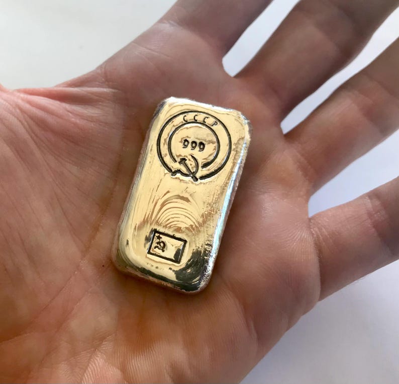 May include: A silver bar with the inscription "CCCP 999" and a hammer and sickle symbol. The bar is in a person's hand.