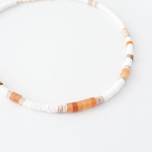 May include: A white and orange beaded necklace with a pattern of small white beads and larger orange beads.