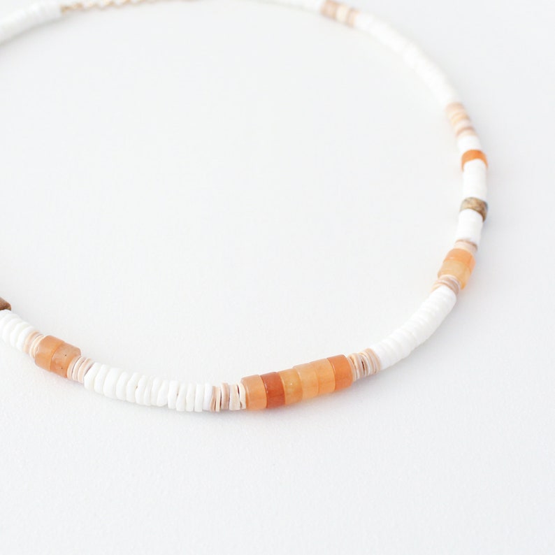 May include: A white and orange beaded necklace with a pattern of small white beads and larger orange beads.