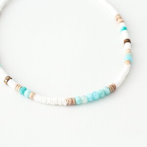 May include: A white, brown, and turquoise beaded necklace with a variety of different sized beads.