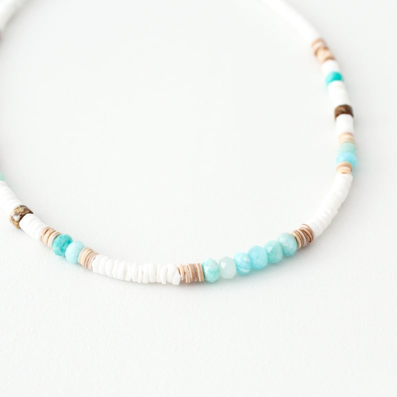 May include: A white, brown, and turquoise beaded necklace with a variety of different sized beads.