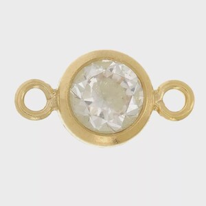Peut inclure: Un connecteur de bijou doré doté d'un sertissage circulaire central contenant une pierre précieuse ronde, transparente et à facettes. Le connecteur possède une petite boucle circulaire de chaque côté pour le fixer à des chaînes.
