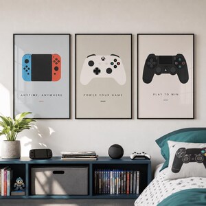 May include: Three framed wall art prints featuring minimalist illustrations of gaming controllers. The left print shows a blue and red handheld console with the text ANYTIME, ANYWHERE. The center print shows a white controller with POWER YOUR GAME. The right print shows a black controller with PLAY TO WIN.