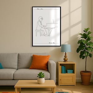 May include: Black framed art print with a line drawing of a person playing a piano. The text "Elton John" is at the top, and "Rocket Man" is at the bottom. The artwork is displayed in a living room setting with a sofa and plant.