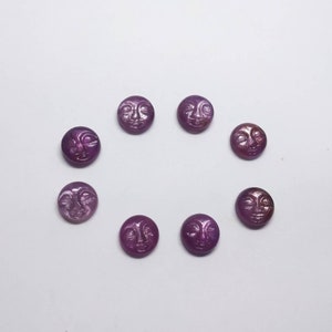 Pode incluir: Oito gemas cabochão roxas com um design de rosto esculpido. As gemas são redondas e têm um acabamento brilhante e iridescente.