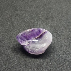 May include: A small, purple amethyst bowl with a smooth, polished surface. The bowl is carved from a single piece of amethyst and has a natural, organic shape.