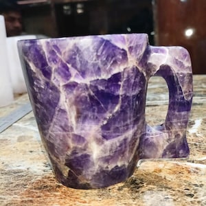 May include: A purple amethyst mug with a handle. The mug is made of natural amethyst crystals and has a unique, organic shape.