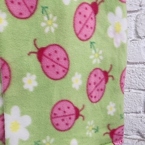 Könnte beinhalten: Grüner Fleece-Stoff mit einem sich wiederholenden Muster aus rosa Marienkäfern und weißen Gänseblümchen.