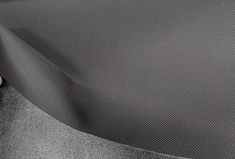 May include: Close-up of a dark gray fabric with a textured weave. The fabric has a subtle sheen and a smooth, soft feel.