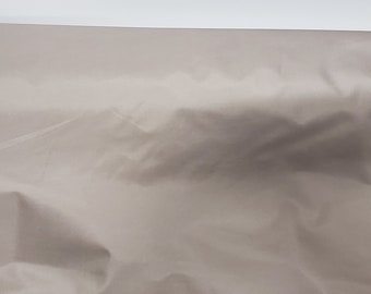 May include: A close-up of a light brown fabric with a smooth texture. The fabric is folded and has a slight sheen.