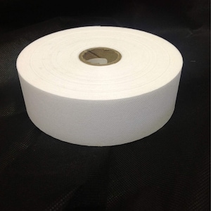 May include: A white roll of fabric tape, wound around a cardboard core. The tape is smooth and has a subtle texture.