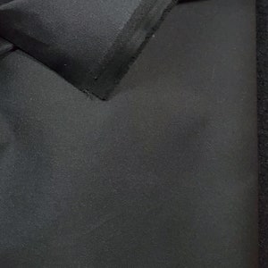 May include: Black fabric with a smooth, slightly textured surface. The fabric is folded over, showing the raw edge.
