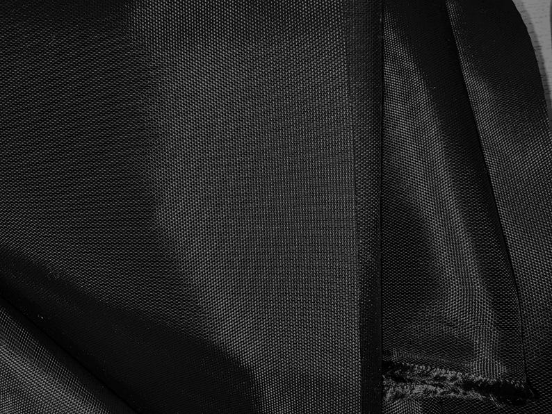 May include: Black fabric with a woven texture. The fabric is folded and shows a seam along the edge.