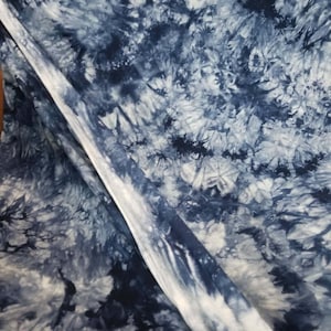 May include: Blue and white tie-dye fabric with a swirling pattern. The fabric is folded in half, showing the pattern on both sides.