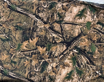 May include: Camouflage fabric with a detailed pattern of branches, leaves, and bark in shades of brown, green, and tan. The design mimics a forest environment, suitable for outdoor apparel or accessories.