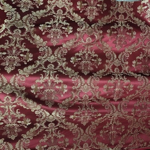 Puede incluir: Tela roja con un patrón de damasco dorado. La tela tiene un brillo sutil y una textura suave.