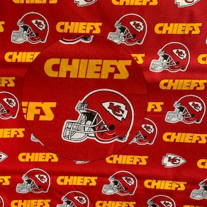 May include: Red fabric with a repeating pattern of the Kansas City Chiefs logo. The logo features a red and white football helmet with a yellow star and the words "Chiefs" in yellow letters.