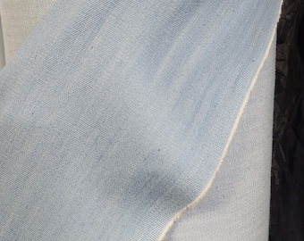 May include: Close-up of a light blue denim fabric with a white seam. The fabric is folded over itself, showing the texture of the denim.
