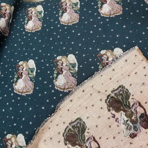 May include: A teal fabric with a repeating pattern of angels playing harps. The fabric has a white star pattern. The fabric is folded over a beige fabric with a similar pattern of angels playing harps.