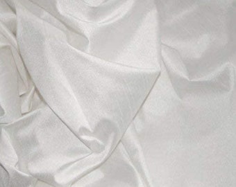 May include: Close-up of a white fabric with a subtle sheen. The fabric is draped and folded, creating shadows and highlights that emphasize its texture. The material appears soft and flowing, with visible vertical lines.