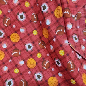 May include: Red fabric with a plaid pattern featuring various sports balls. The design includes footballs, soccer balls, basketballs, baseballs, and tennis balls. The balls are in shades of brown, orange, white, and yellow.
