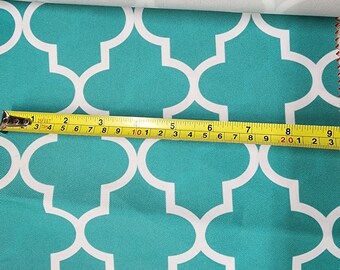 May include: A teal fabric with a white geometric pattern. A yellow measuring tape is placed on top of the fabric, showing a measurement of 9 inches.