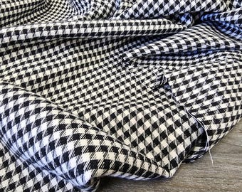May include: Black and white checked fabric with a woven texture. The fabric is folded and draped, showing the pattern and texture.