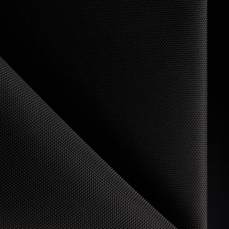 May include: Close-up of a black fabric with a textured weave. The fabric is folded in half, creating a diagonal line.