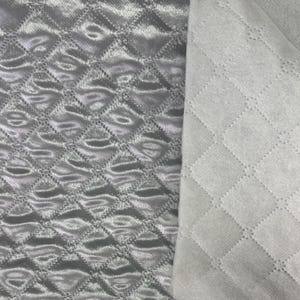 May include: Two sections of quilted fabric are shown. One is a shiny, silvery-gray material with a diamond pattern. The other is a matte, off-white fabric with the same diamond quilting. The fabrics are likely used for bedding or upholstery.
