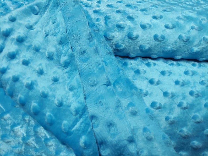 K&ouml;nnte beinhalten: Nahaufnahme eines weichen, blauen Stoffes mit einem strukturierten, gepunkteten Muster. Der Stoff ist gefaltet und zeigt die Textur der Punkte.