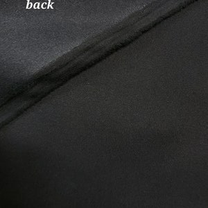 May include: Close-up of black fabric with a smooth, shiny texture on one side and a textured, woven texture on the other side. The word "back" is written on the smooth side.
