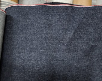 May include: Close-up of a dark blue denim fabric with a red selvedge edge.