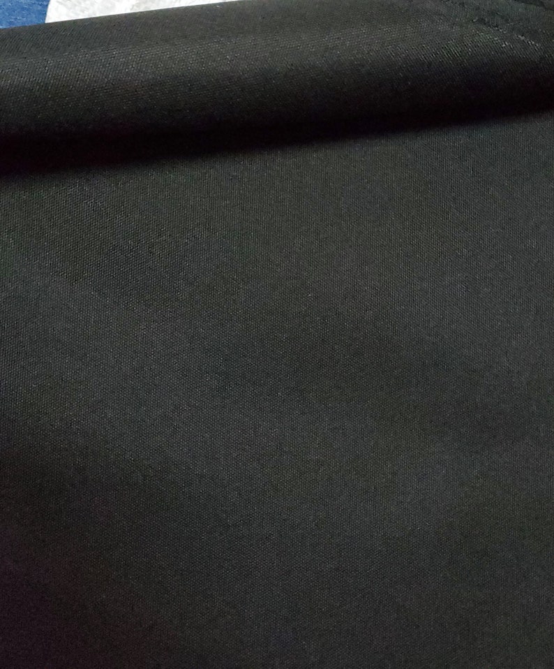 May include: Close-up of a black fabric with a woven texture. The fabric is folded over, showing the underside.