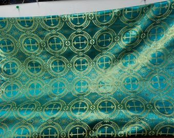 Op de afbeelding: Turquoise stof met een gouden kruispatroon. De stof heeft een herhalend patroon van gouden kruisen in cirkels.