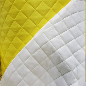 May include: A close-up of two pieces of quilted fabric. One piece is yellow and the other is white. Both pieces have a diamond pattern.