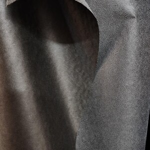 May include: Close-up of black fabric with a textured surface. One side of the fabric has a smooth, woven texture, while the other side has a fine, dotted texture.