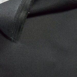 May include: Close-up of a black fabric with a woven texture. The fabric is folded over, showing the underside.