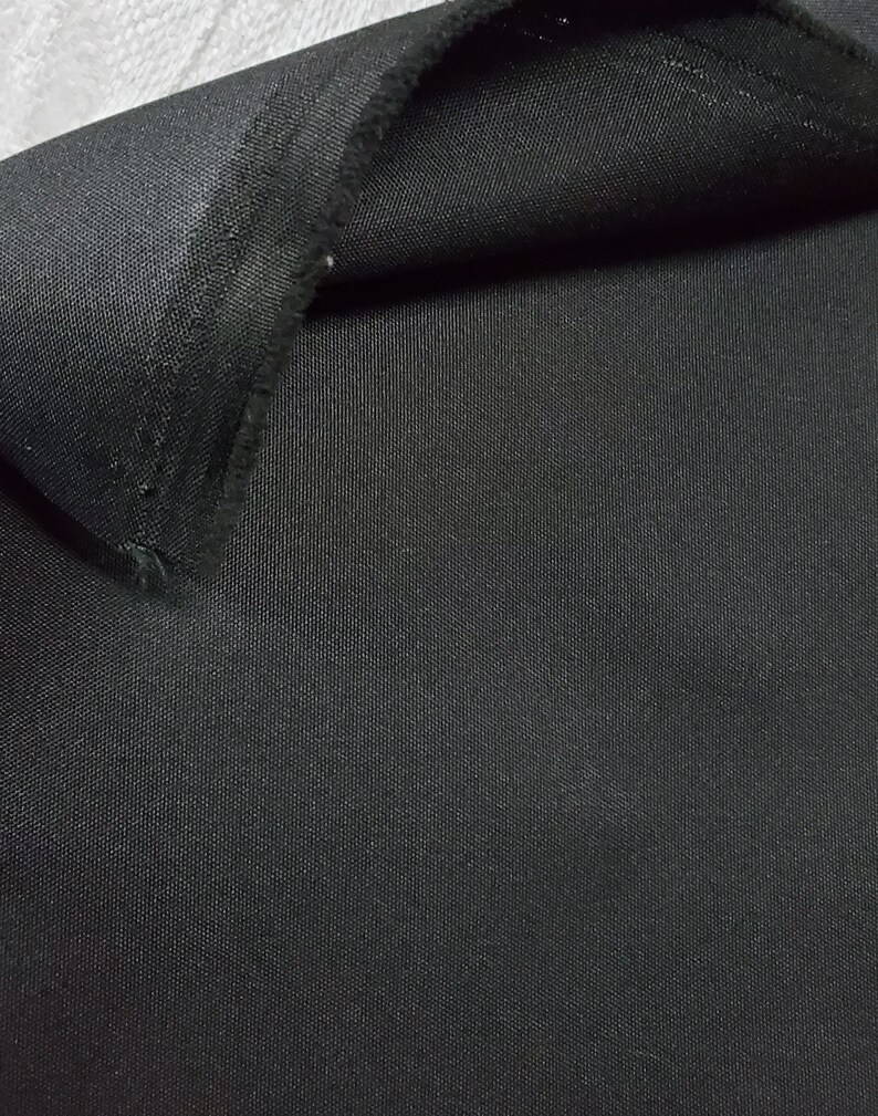 May include: Close-up of a black fabric with a woven texture. The fabric is folded over, showing the underside.