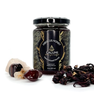 Puede incluir: Un tarro de vidrio de miel de hibisco con una etiqueta negra que dice "Hibiscus Honey", "Lalumi", "Enhance your inner light", "Herb-infused Honey", "Fragrant and cooling Hibiscus" y "8 oz. (237 ml)".