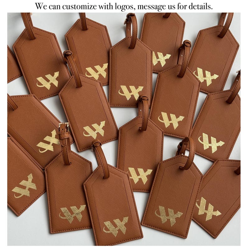 Puede incluir: Etiquetas de equipaje marrones con logotipos "W" dorados. Cada etiqueta tiene una correa y una hebilla a juego. Las etiquetas est&aacute;n dispuestas en un patr&oacute;n disperso. El texto "We can customize with logos, message us for details" es visible.