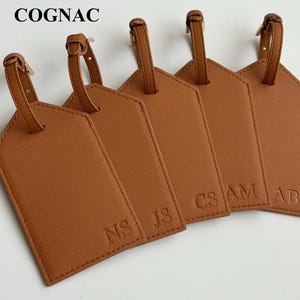 May include: Five cognac-colored luggage tags with matching straps. Each tag has a different set of initials embossed on the front: NS, JS, CS, AM, and AB. The word "COGNAC" is printed at the top.