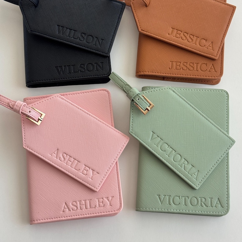 May include: Four sets of passport holders and matching luggage tags in black, tan, pink, and sage green. Each item features a textured finish and is embossed with names: Wilson, Jessica, Ashley, and Victoria. Each tag has a gold-tone buckle.