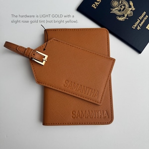 May include: A brown passport holder and luggage tag with the name "SAMANTHA" embossed on them. The luggage tag has a light gold buckle. A United States passport is visible in the background.